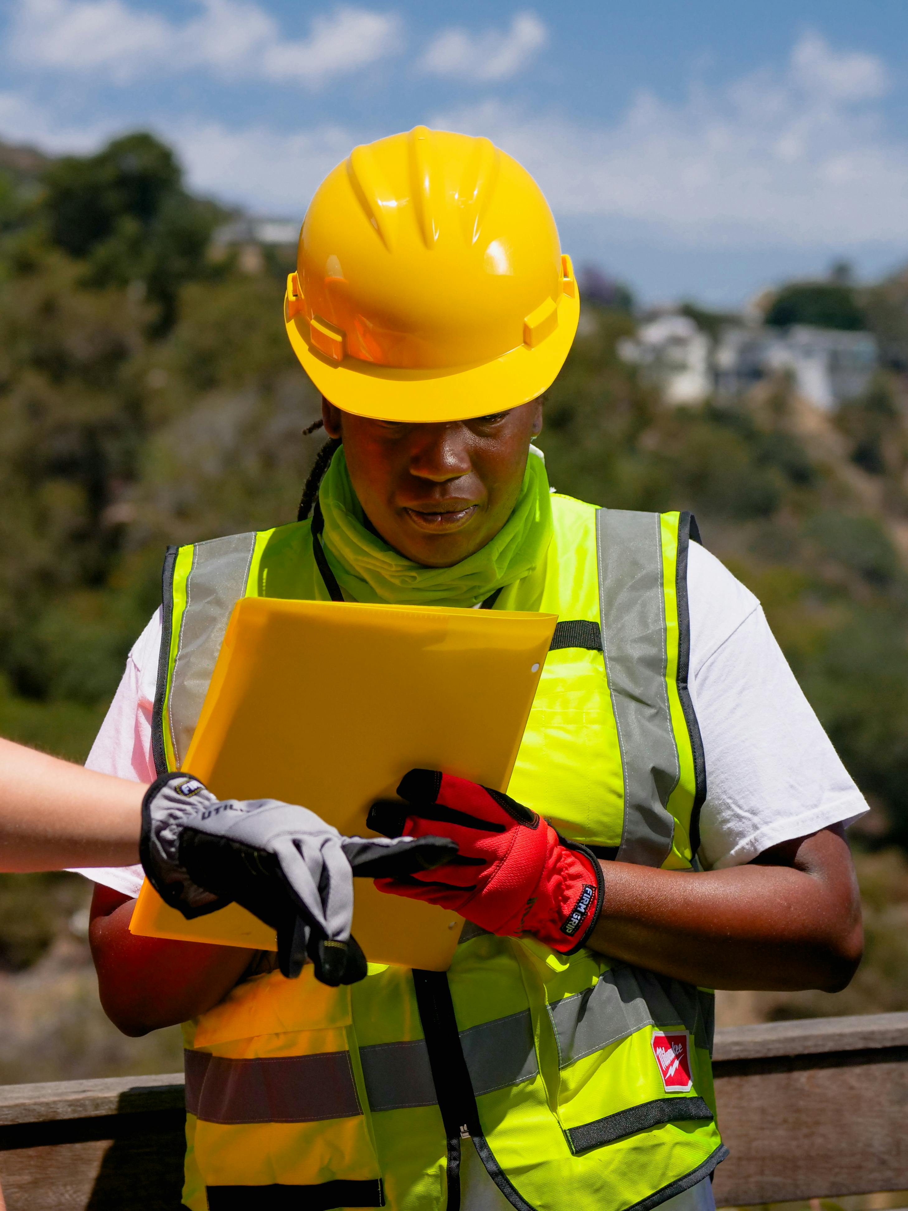 Female construction worker reviewing plans with safety gear in a sunny outdoor setting.